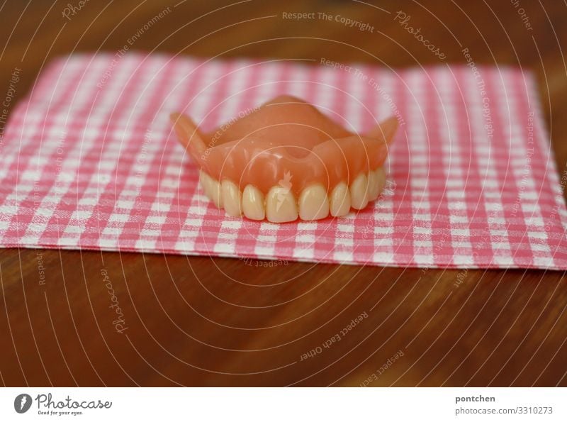 Zahngesundheit. Gebiss der oberen Zähne liegt auf einem rosa-weiß karierten Tuch Zahnarzt einzigartig lustig Hälfte Serviette Senior kaputt Karies Lächeln