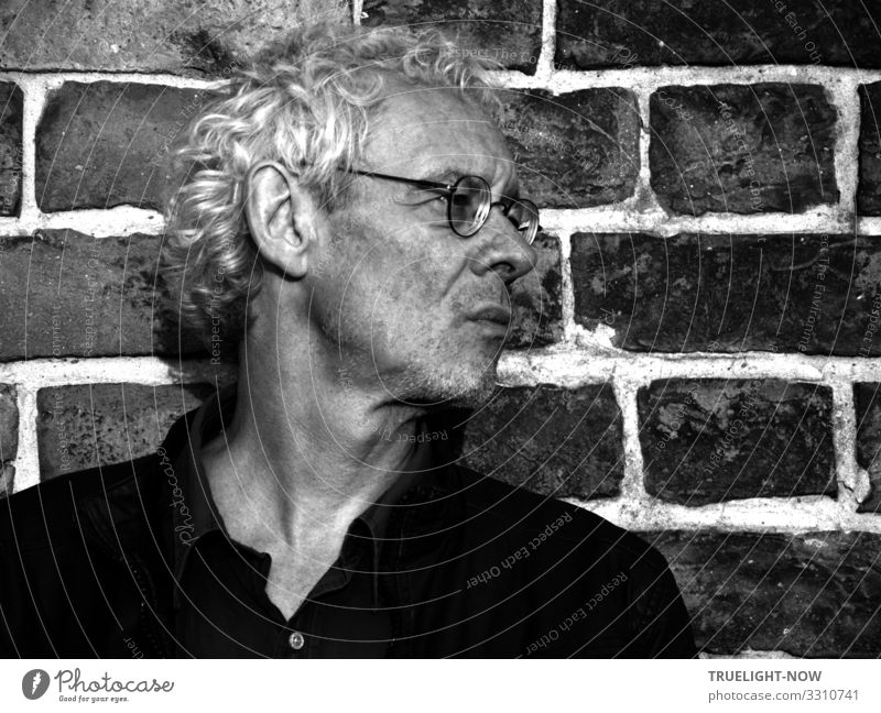 Nicht abgehoben | Bekannte Photocase Ikone, Senior User, Mann mit Brille zu Besuch in Potsdam vor einer Backstein Wand im schwarz/weiss Profil mit silbernen Locken, schwarzem Polo Shirt, Blick streng nach rechts