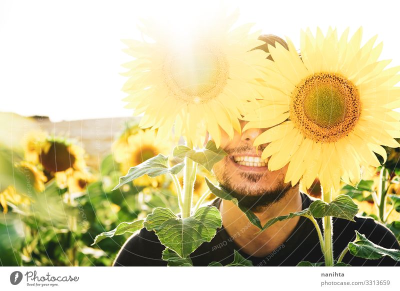 Junger Mann genießt den Tag auf einem Sonnenblumenfeld Gesicht Leben Mensch maskulin Erwachsene Natur Frühling Wetter Schönes Wetter Blume Vollbart genießen