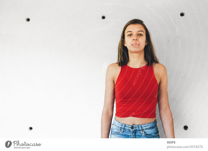Teenager-Mädchen bläst eine Kaugummiblase gegen eine Betonwand Freude schön Gesicht Frau Erwachsene Jugendliche brünett niedlich rot weiß Gefühle trotzig