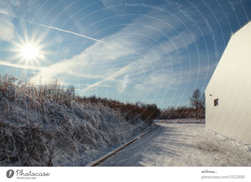 Sonnige Winterlandschaft mit Hauswand Schnee Straße kalt Sonnenstrahlen Kondensstreifen Schönes Wetter Sträucher Wand Gebäude Wolken Landschaft winterlich