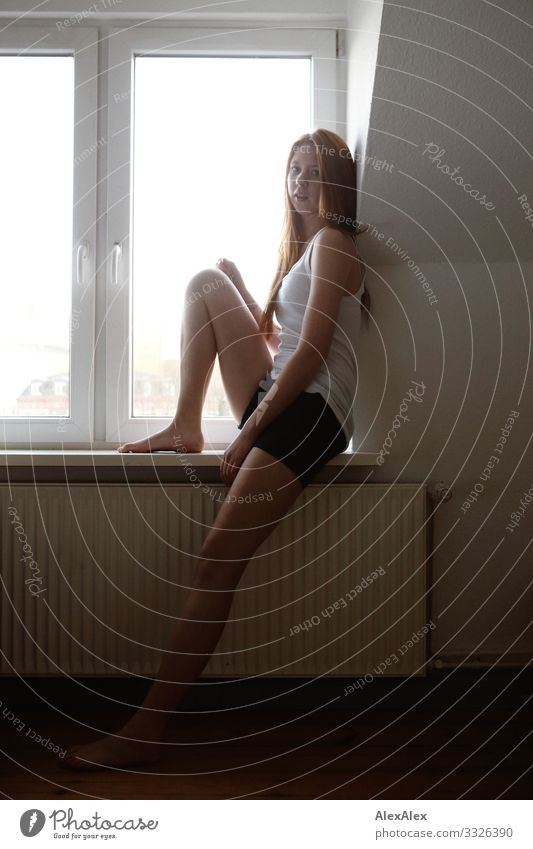 Junge Frau sitzt am Fenster Lifestyle schön Wohlgefühl Häusliches Leben Wohnung Heizkörper Jugendliche Beine 18-30 Jahre Erwachsene Hotpants Hemd Barfuß