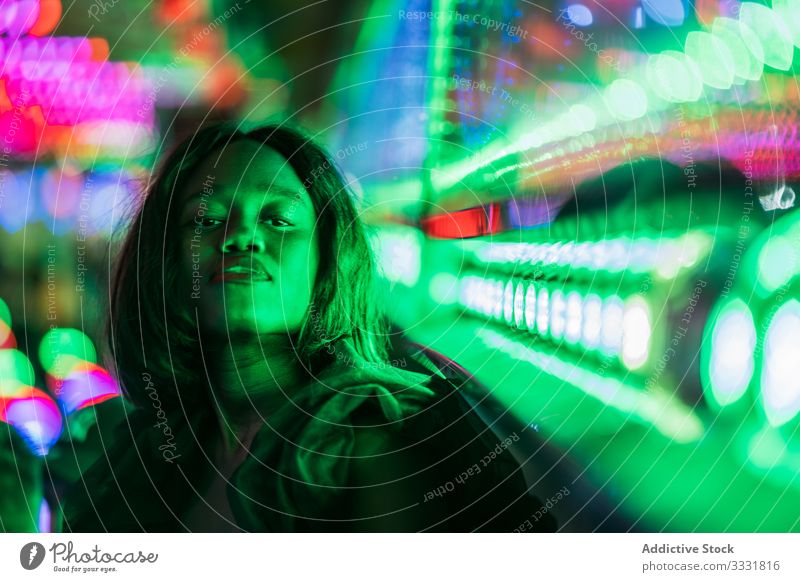 Fröhliche schwarze Frau auf Rummelplatz Jahrmarkt Lächeln Nacht Arkaden Illumination sitzen ruhen Wochenende ethnisch Vergnügen Anziehungskraft farbenfroh
