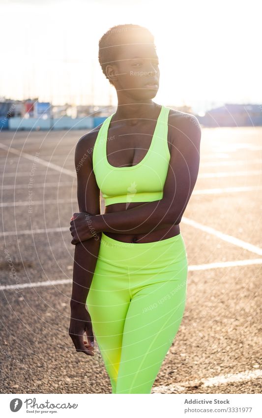 Zuversichtliche ethnische Sportlerin vor dem Training auf dem Sportplatz bei Sonnenuntergang selbstbewusst Motivation Straße Fokus ernst Physis schlank