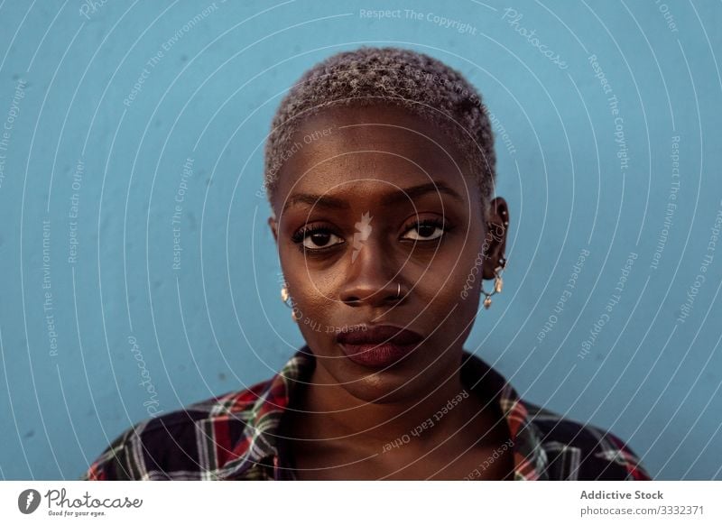 Junge, schwarze, kurzhaarige Frau schaut mit intensivem Blick in die Kamera traurig Porträt Herausforderung Kurze Haare Piercing kariertes Hemd Afroamerikaner