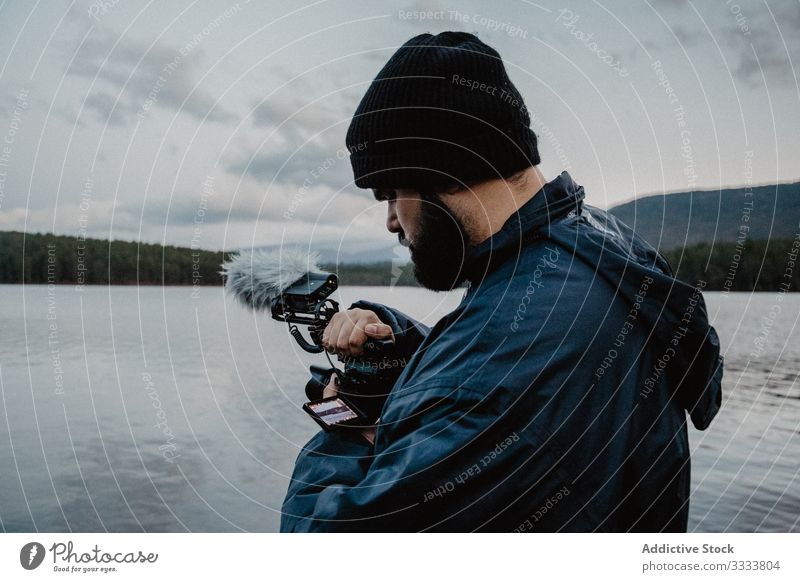 Fokussierter Mann betrachtet Fotos vor der Kamera benutzend Fotokamera Videofilmer überblicken Fluss Wald Natur fokussiert beschäftigt ernst Strand männlich