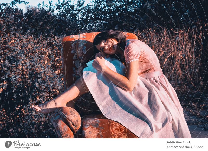 Verträumte Frau auf einem Sessel auf dem Land Landschaft verträumt Armsessel Konzept stylisch Komfort Barfuß Kleid niedlich jung Natur Buchse Strauch Denken