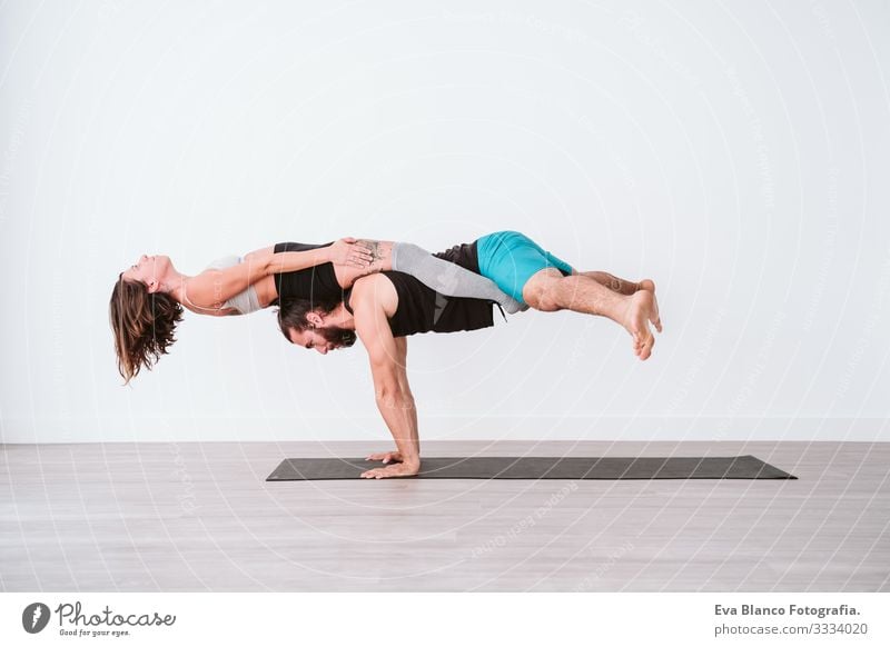 junges Paar, das in einem weißen Studio oder einer Sporthalle Akro-Yoga praktiziert. Gesunder Lebensstil im Innenbereich Gesundheit Mann Kraft Mensch