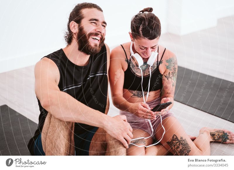 zwei Freunde im Fitnessstudio, die über Handy und Headset Musik hören und Spaß haben. Sport- und Technologiekonzept Paar Freundschaft Jugendliche Mann Frau