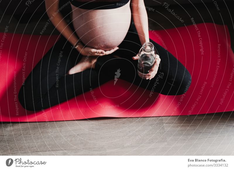 junge schwangere Frau, die zu Hause Yoga-Sport und Trinkwasser praktiziert, gesunde Lebensweise heimwärts Gesundheit Lifestyle Jugendliche Kaukasier