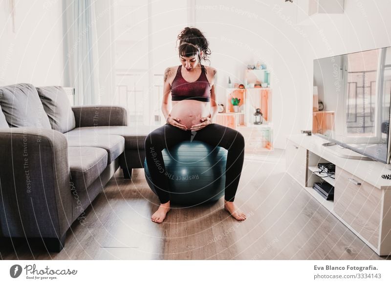 junge schwangere Frau zu Hause auf Pilates-Ball sitzend, gesunde Lebensweise Yoga heimwärts Sport Gesundheit Lifestyle Jugendliche Kaukasier Kindererziehung