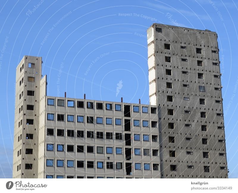 leerstehendes Bürogebäude kurz vor dem Abriss Abrissgebäude Hochhaus Beton hoch grau blau Himmel schwarz Ruine Bauruine entkernt fensteröffnung Gebäude schmal
