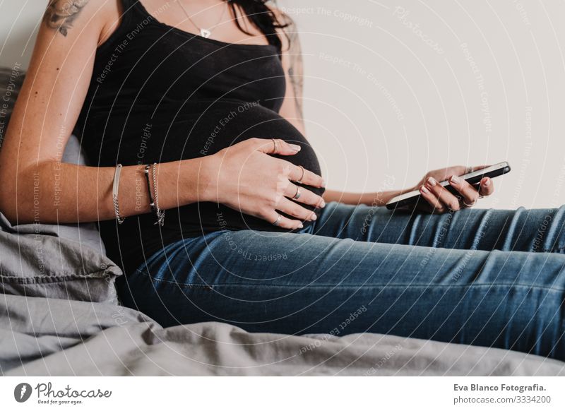 junge schwangere Frau, die zu Hause ein Mobiltelefon benutzt Funktelefon Technik & Technologie benutzend heimwärts Bett PDA erwartend Baby bauchfrei Internet