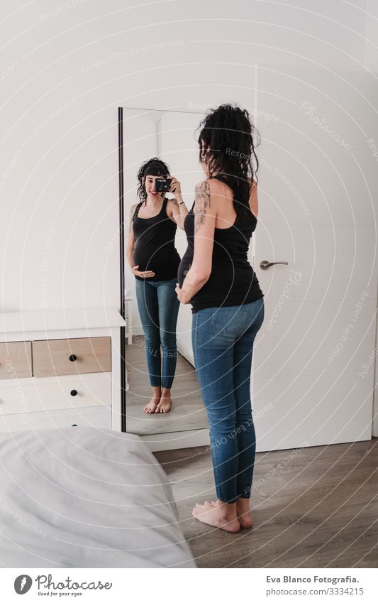 junge schwangere Frau zu Hause, die sich mit der Kamera auf den Spiegel stellt Grafik u. Illustration Fotokamera heimwärts Lächeln Glück Porträt Jugendliche