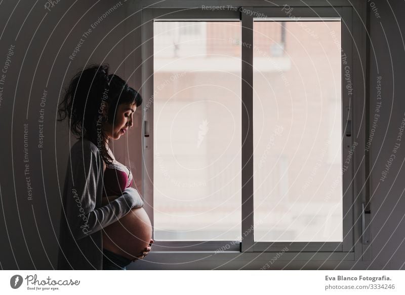 Porträt einer jungen schwangeren Frau, die zu Hause am Fenster steht heimwärts Lifestyle erwartend Tag Leben Erwartung Beautyfotografie Kindererziehung