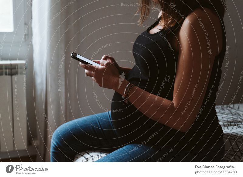 junge schwangere Frau zu Hause, die ein Mobiltelefon benutzt heimwärts Handy Technik & Technologie PDA Lächeln bauchfrei dick Baby erwartend Innenaufnahme