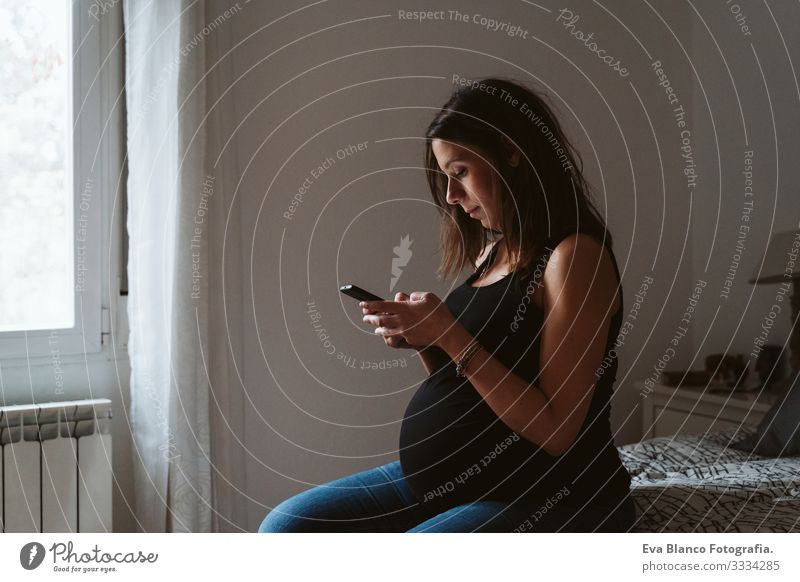 junge schwangere Frau, die zu Hause ein Mobiltelefon benutzt heimwärts Funktelefon Technik & Technologie PDA Lächeln bauchfrei Fett Baby erwartend Innenaufnahme