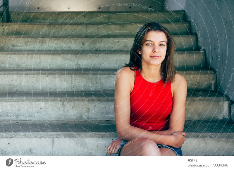 Porträt eines schönen und selbstbewussten Teenager-Mädchens in rotem Top und Jeansrock, das auf der Treppe im Freien sitzt und lächelt Lifestyle Glück Sommer