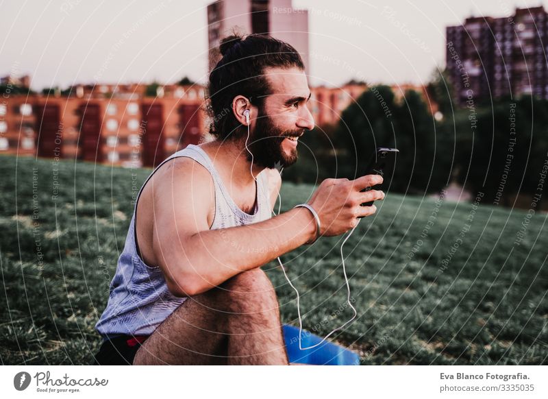junger Mann in einem Park, der nach der Ausübung von Yoga-Sport Musik über Handy und Headset hört. städtischer Hintergrund. gesunder Lebensstil.
