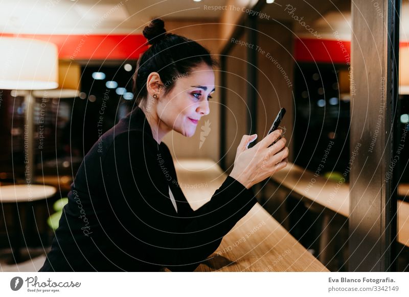 eine junge Frau, die in einem Café oder Restaurant in Innenräumen ein Mobiltelefon benutzt. Technologie und Lebensstil Handy Innenaufnahme Fenster Geschäftsfrau