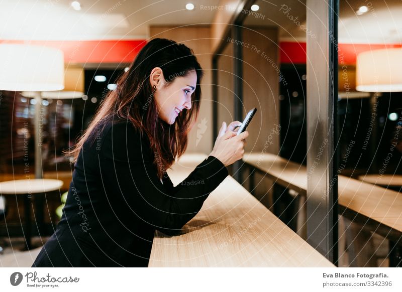 eine junge Frau, die in einem Café oder Restaurant in Innenräumen ein Mobiltelefon benutzt. Technologie und Lebensstil Handy Innenaufnahme Fenster Geschäftsfrau