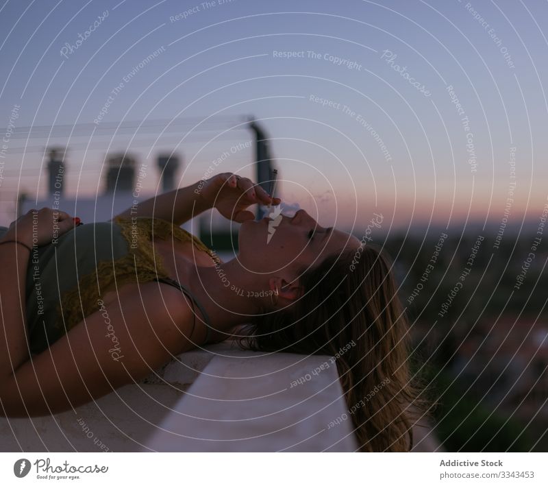 Gelassene Frau entspannt sich bei einer Zigarette auf dem Balkon sich[Akk] entspannen Rauchen geschlossene Augen Lügen aussruhen Zaun Terrasse Sonnenuntergang