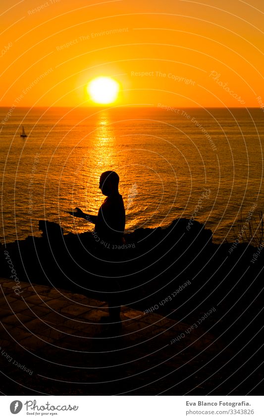 Silhouette eines jungen Mannes, der bei Sonnenuntergang ein Mobiltelefon benutzt. Hintergrund: Ozean. Urlaubs- und Technologiekonzept Jugendliche Hand