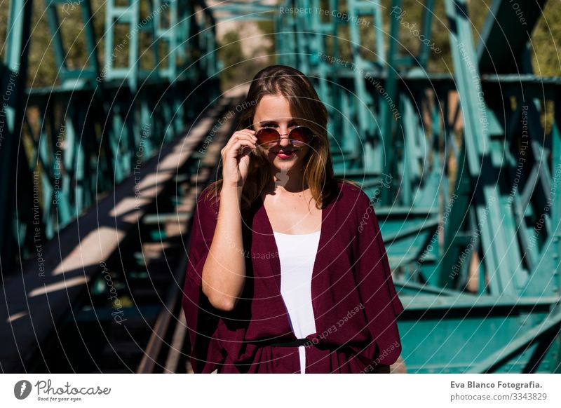 Porträt einer jungen schönen Frau auf einer grünen Brücke. Stilvolle Kleidung zu tragen. Sonnenbrille halten. Fallstil. Im Freien. Sonnig Eisenbahn hübsch