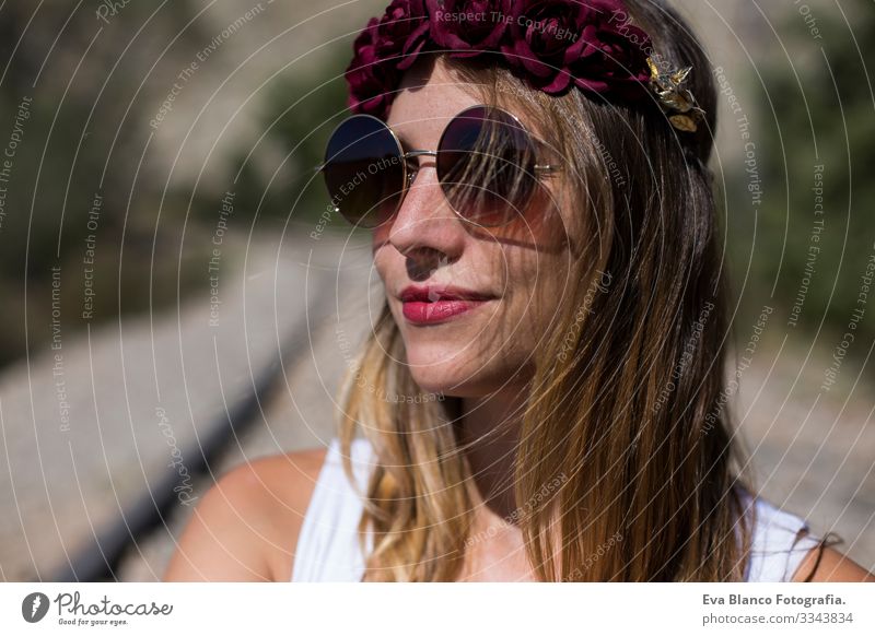 Nahaufnahme eines Porträts einer jungen schönen Frau mit einer modernen Sonnenbrille und einem roten Rosenkranz auf dem Kopf. Im Freien. Sonnig. Lebensstil