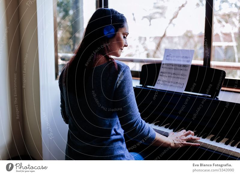 junge Frau, die beim Klavierspielen ein Notenblatt in der Hand hält. Musikkonzept im Innenbereich. Rückansicht Stil Mensch Schlüssel Hinweis Schulunterricht