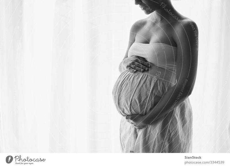 Junge schöne schwangere Frau am Fenster stehend Lifestyle Glück Körper Leben Mensch Baby Erwachsene Mutter Hand Kleid berühren Liebe sitzen schwarz weiß