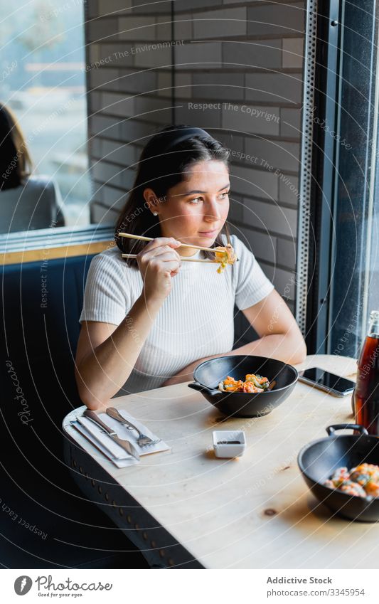 Nachdenkliche Frau mit Essstäbchen in der Hand beim Mittagessen in einem asiatischen Café Asiatische Küche benutzend Essen Sitzen Tisch lässig Gemüse speisend