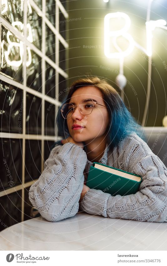 Frau mit blauen Haaren, die in einem Café ein Buch hält Erwachsene Beautyfotografie bunte Haare niedlich Bildung Gesicht Junge Frau Halt Innenaufnahme