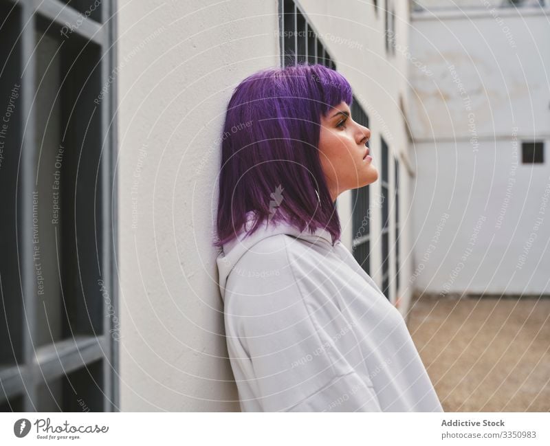 Nachdenkliche Frau mit lila Haaren in weißem Kapuzenpulli an der Wand lehnend Lehnen stylisch urban purpur Frisur selbstbewusst Mode jung Sackgasse Stil