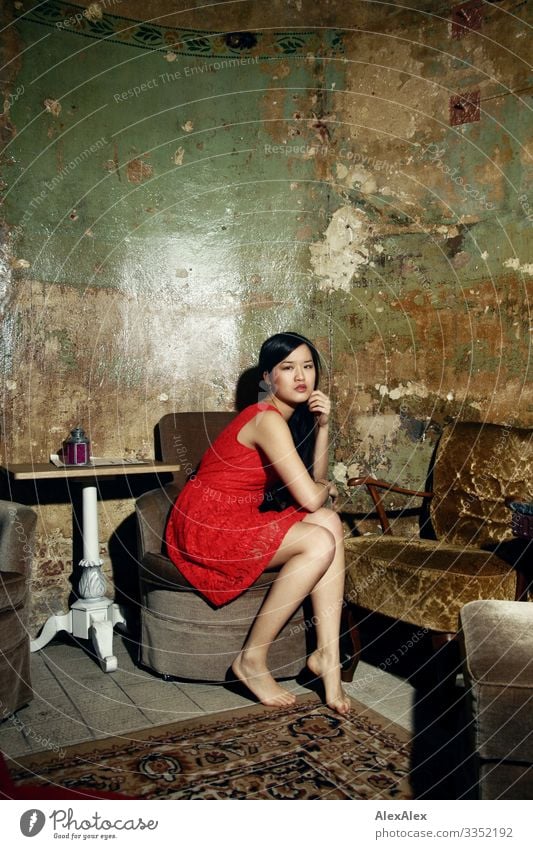 Junge Frau in rotem Kleid auf einem Sessel Stil Freude schön Leben Tisch Raum Wohnzimmer Jugendliche Beine 18-30 Jahre Erwachsene Barfuß schwarzhaarig
