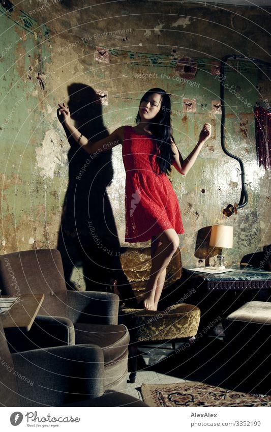 Portrait einer jungen Frau in rotem Kleid auf einem Sessel Stil Freude schön Leben Wohnzimmer Junge Frau Jugendliche 18-30 Jahre Erwachsene rotes Kleid Barfuß