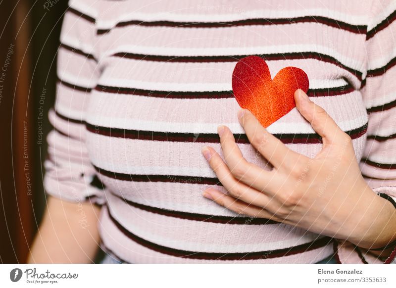 Frau mit rotem herzförmigem Karton in Brustnähe. Feste & Feiern Valentinstag Büroarbeit Mensch Erwachsene Jugendliche Frauenbrust Hand Herz Liebe tragen