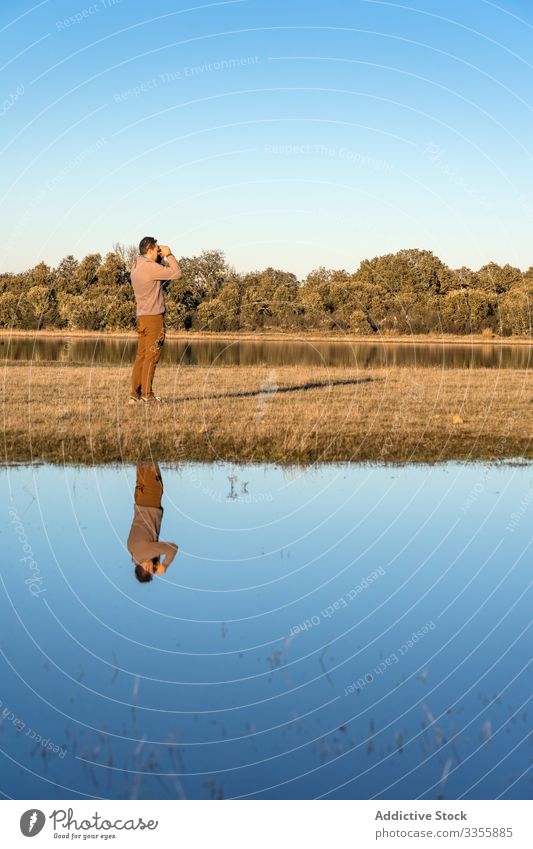 Anonymer Mann schaut auf ein Fernglas in einer Lagune Wasser Landschaft Wald See Feuchtgebiet Abenteuer wild Fauna Blauer Himmel sonnig malerisch Textfreiraum