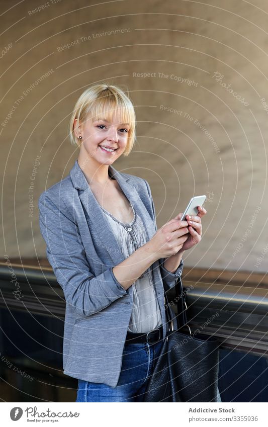 Lächelnde Geschäftsfrau mit Smartphone stylisch jung heiter Geländer Frau professionell Person schön benutzend Browsen in die Kamera schauen attraktiv