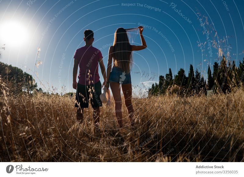 Verspielter junger Mann steht mit Frau im Feld mit Hut in der Hand Freund spielen Natur reisen Abenteuer Aktivität Zusammensein spielerisch Himmel Freiheit