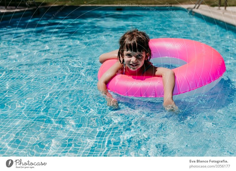 Hübsches Mädchen, das auf rosa Donuts in einem Pool schwimmt. Sonnenbrille tragen und lächeln. Spaß und sommerlicher Lebensstil Aktion Schwimmbad