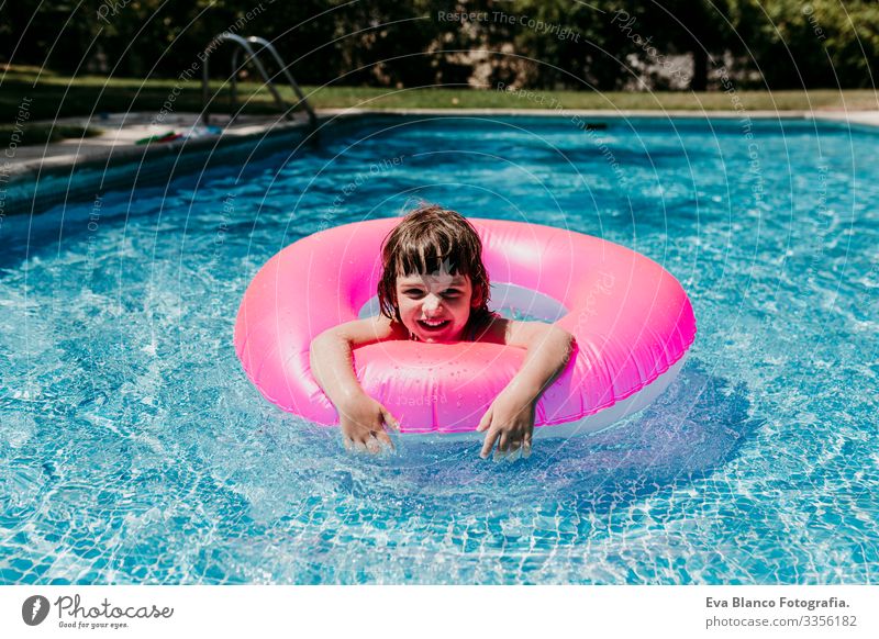 Hübsches Mädchen, das auf rosa Donuts in einem Pool schwimmt. Lächelnd. Spaß und sommerlicher Lebensstil Aktion Schwimmbad Beautyfotografie Außenaufnahme