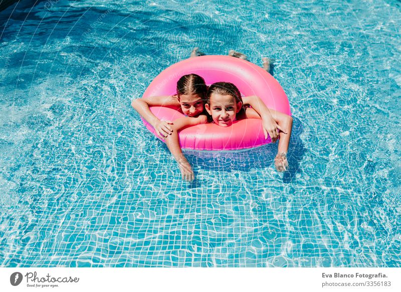 zwei wunderschöne Teenager-Mädchen, die auf rosa Donuts in einem Pool schwimmen. lächelnd. Spaß und sommerlicher Lebensstil Aktion Schwimmbad Außenaufnahme