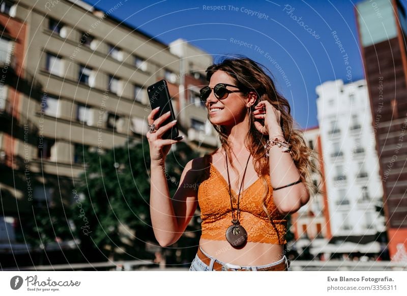 Hübsche junge kaukasische Frau, die an einem sonnigen Tag auf der Straße der Stadt spazieren geht. Sprechen mit dem Mobiltelefon. Glückliches Gesicht lächelt. Urbaner Lebensstil
