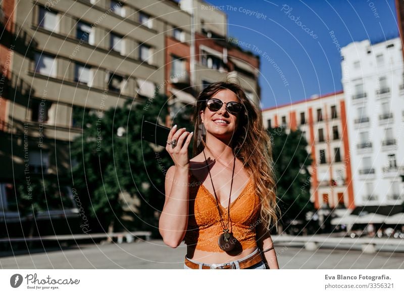 Hübsche junge kaukasische Frau, die an einem sonnigen Tag auf der Straße der Stadt spazieren geht. Senden eines Audios mit dem Mobiltelefon. Glückliches Gesicht lächelt. Urbaner Lebensstil