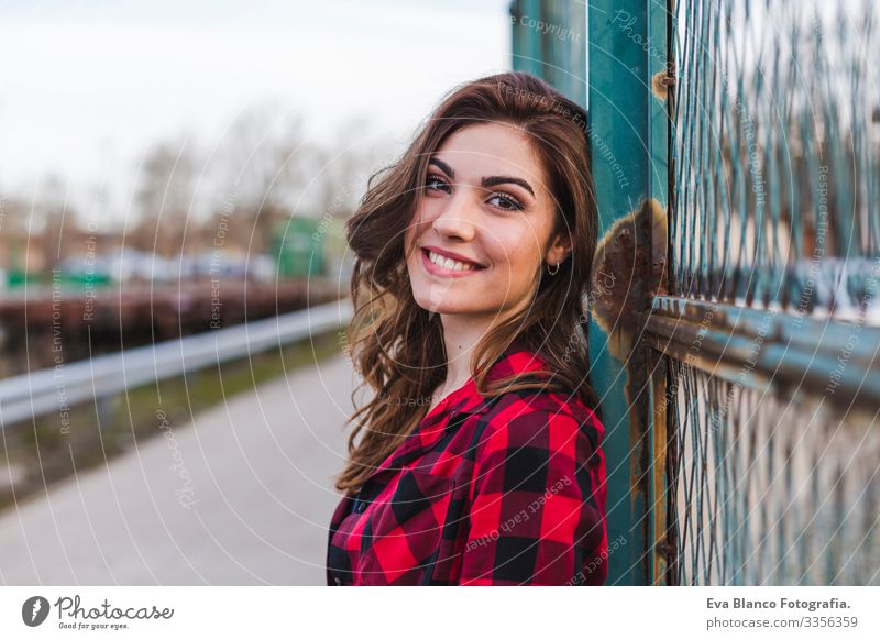 junge schöne Frau, die an einem Zaun steht. Sie trägt lässige Kleidung und lächelt. Hintergrund der Stadt im Freien. Lebensstil Hut stehen attraktiv Mobile