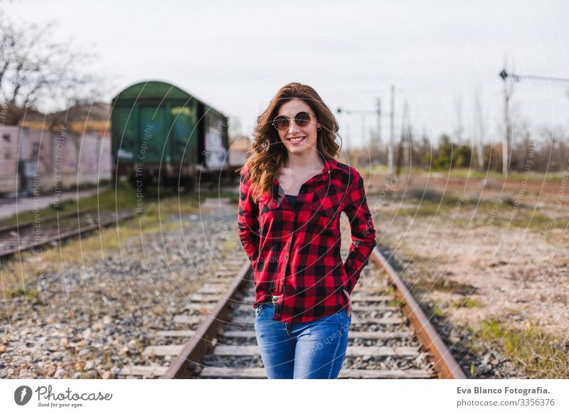 eine junge, schöne Frau in legerer Kleidung, die an der Eisenbahn vorbeikommt und lächelt. Lebensstil im Freien. Reisekonzept. Großstadt Außenaufnahme feminin