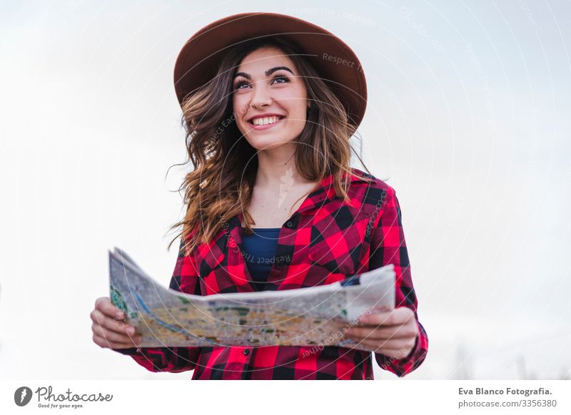 Nahaufnahme eines Porträts einer jungen, schönen Frau in legerer Kleidung, mit Blick auf eine Landkarte und mit einem modernen Hipster-Hut. Spaß und Lebensstil im Freien. Reisekonzept.