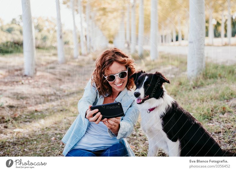 Frau und schöner Border-Collie-Hund, der in einem Pfad von Bäumen im Freien sitzt. Frau, die einen Selfie mit dem Handy mitnimmt Border Collie Außenaufnahme