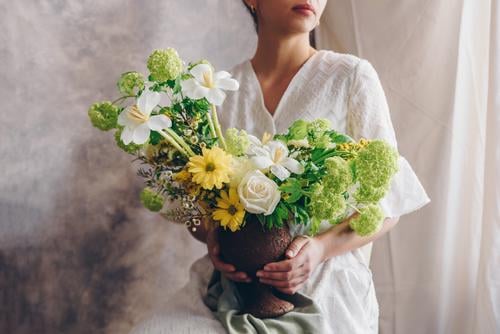 Junge Frau in einem weißen Kleid, die eine Vase mit Blumen hält. Lifestyle elegant Stil Glück schön Stuhl Hochzeit Erwachsene Lippen Hand brünett Blumenstrauß